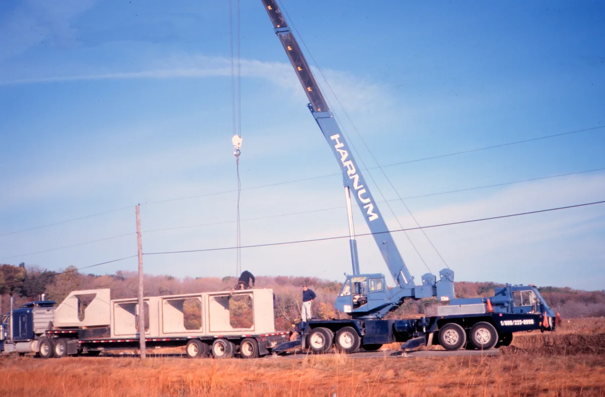 Mobile crane unloading culvert sections from a flatbed truck